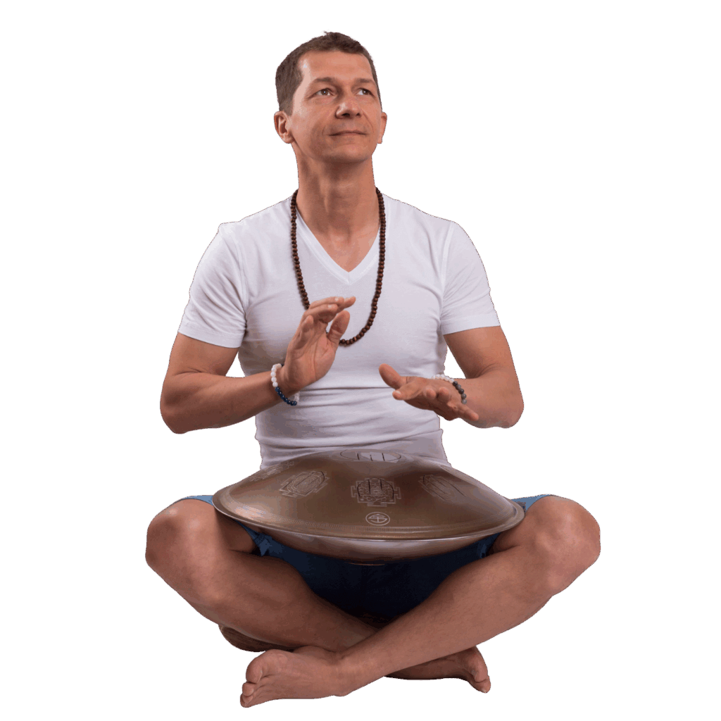 Hangutazás kézidobbal – intuitív zenélés és belső utazás férfi vezetésével Egy meditáló férfi fehér pólóban és lótuszülésben kézzel játszik egy fém hangdobon, hangutazás közben, nyugodt, elmélyült arckifejezéssel